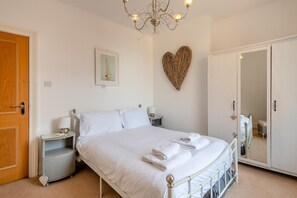Une chambre à coucher avec un lit, des tables de chevet, un miroir, un lustre et une décoration en forme de cœur accrochée au mur.