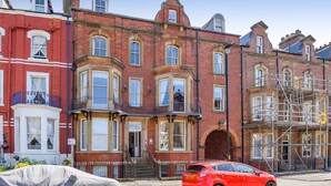 A row of red brick townhouses with bay windows, a red car parked in front, and scaffolding on the right side. - 2 Bed in Whitby (oc-w1028) (Whitby)