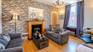 A living room with a fireplace, a sofa, a coffee table, and a dining area with a table and chairs. - 2 Bed in Whitby (oc-w1028) (Whitby)
