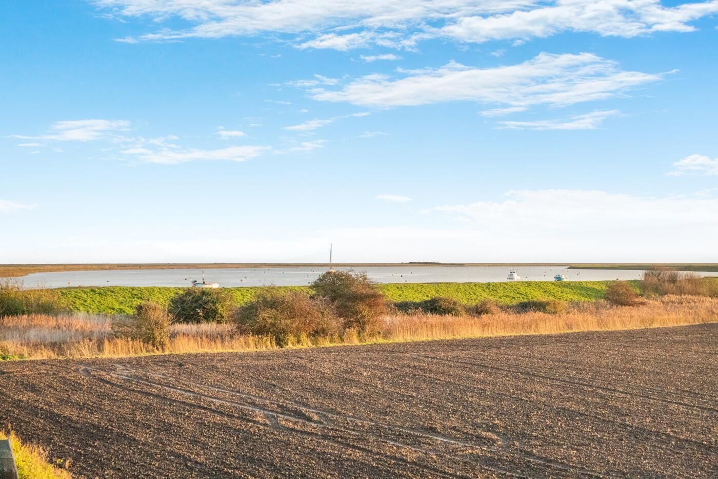 A wide view of a coastal landscape with a field in the foreground and a body of water in the background.