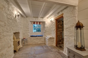 A stone-walled room with a window, a stone bench, a small table, and a wall-mounted light fixture. - 3 Bed in St. Just (oc-p00674) (Carnyorth)