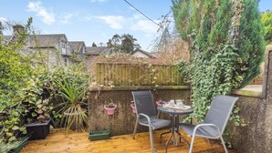 A wooden deck with two chairs and a table, surrounded by potted plants and a wooden fence. - 2 Bed in Grasmere (oc-ld175) (Grasmere)