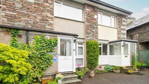A two-story stone building with a white door and windows, surrounded by greenery and potted plants. - 2 Bed in Grasmere (oc-ld175) (Grasmere)