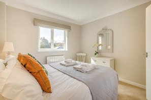 A bedroom with a bed, a window, a radiator, a dresser, and a mirror.