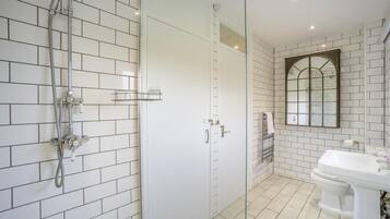 A bathroom with white tiled walls, a shower with a handheld showerhead, a toilet, and a sink.