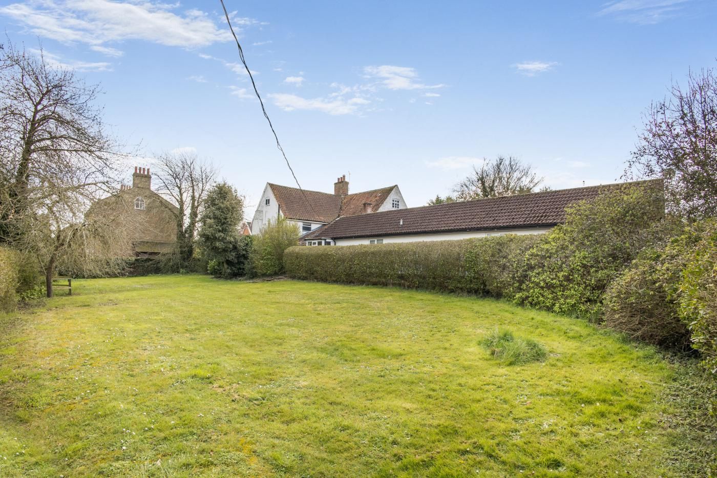 A grassy yard with a house and a hedge.