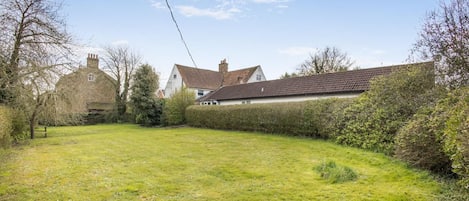 A grassy yard with a house and a hedge.
