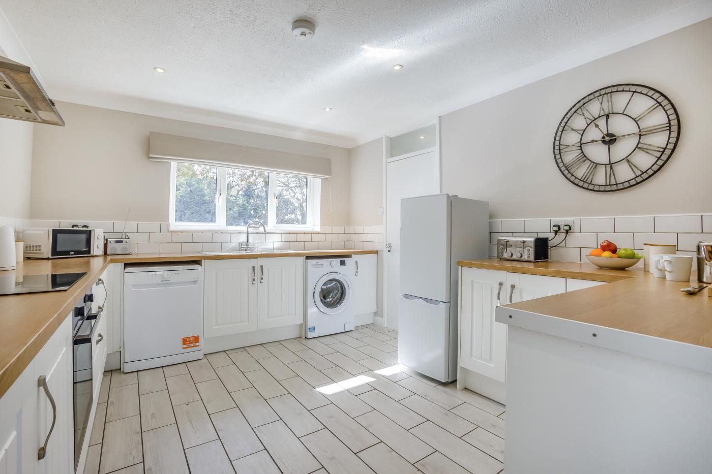 A modern kitchen with white cabinetry, a washing machine, a refrigerator, and a clock on the wall.