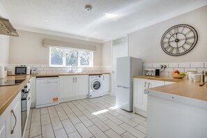 Une cuisine moderne avec des meubles blancs, un lave-linge, un réfrigérateur et une horloge au mur.