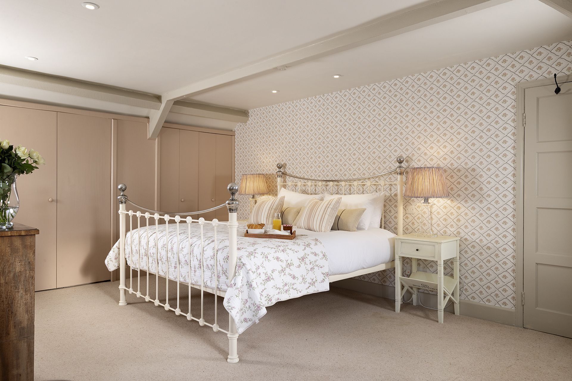 A bedroom with a bed, bedside tables, a lamp, and a vase of flowers.