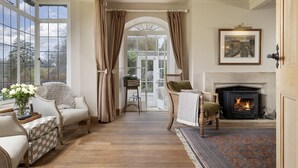 Een gezellige woonkamer met een open haard, een groot raam met gordijnen en uitzicht op de omgeving.