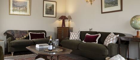 A cozy living room with a green sofa, a coffee table with a bottle of champagne, and a globe on a side table.