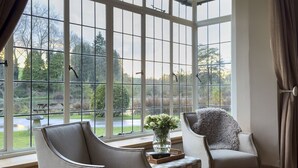 Een kamer met grote ramen, twee fauteuils, een tafeltje en een bloemenvaas.