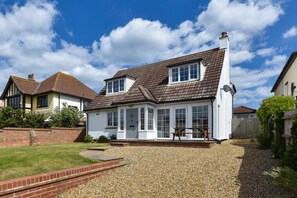 A two-story house with a large front porch, a gravel driveway, and a brick wall. - 4 Bed in Sheringham (oc-2330) (Sheringham)