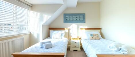A bedroom with two single beds, a radiator, a window with blinds, and a wall-mounted light switch panel.