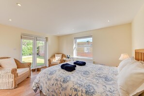 A bedroom with a large bed, a wicker chair, a small table, and a window. - 4 Bed in Sheringham (oc-2330) (Sheringham)