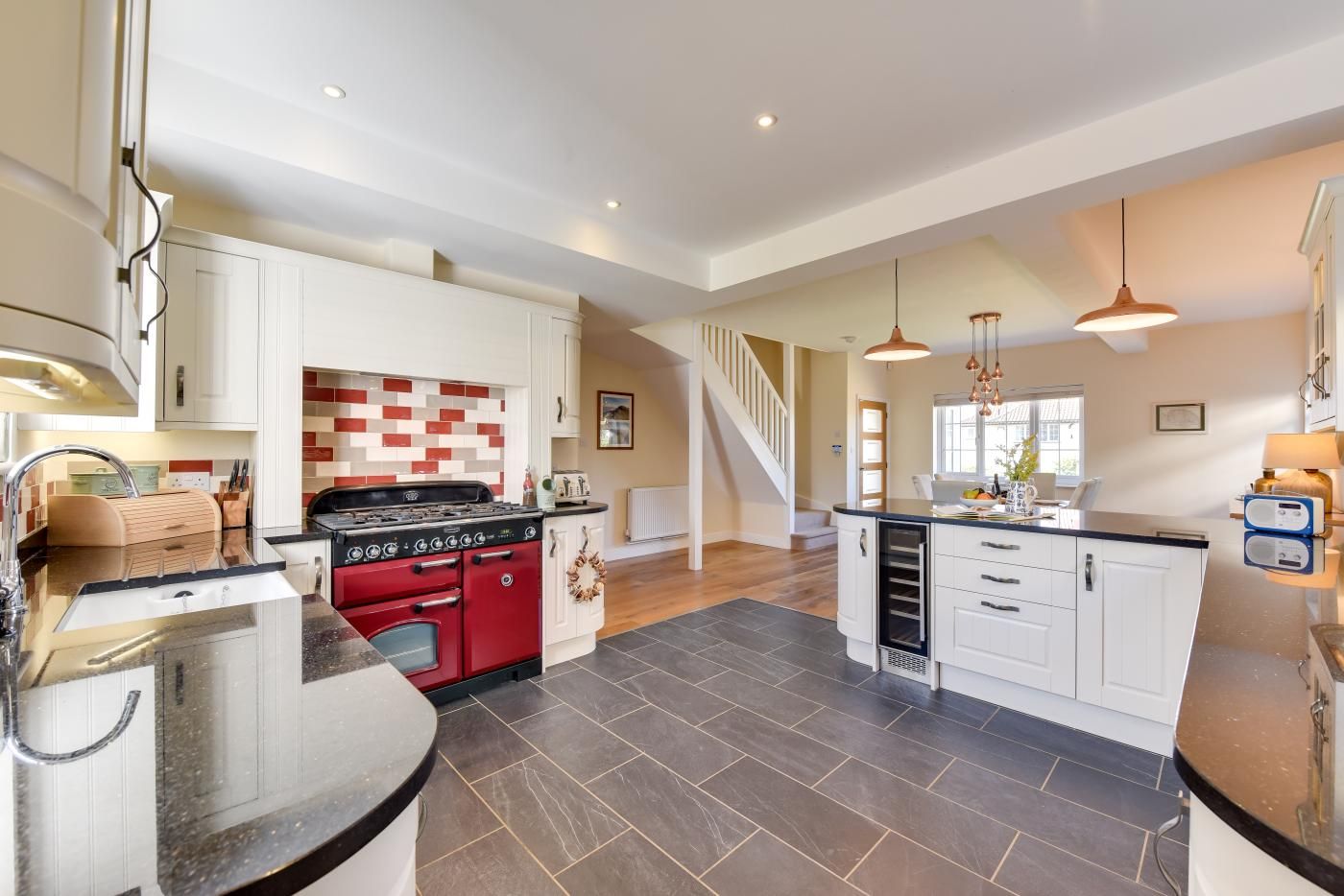 A spacious kitchen with a central island, a red stove, white cabinetry, and a modern pendant light.