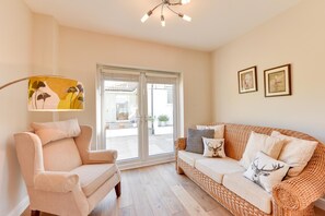 Ein Wohnzimmer mit Sofa, Sessel und einem großen Fenster mit Blick ins Freie.