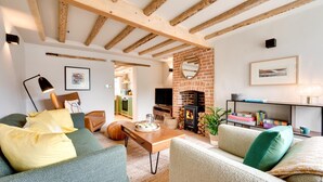A cozy living room with exposed wooden beams, a brick fireplace, and a comfortable seating area with cushions. - 2 Bed in Castle Acre (oc-2307) (Castle Acre)