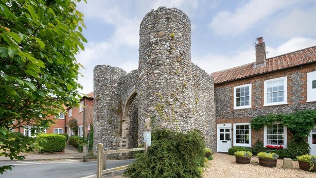 A historic stone tower with a cobblestone path leading to a traditional brick building with a white door. - 2 Bed in Castle Acre (oc-2307) (Castle Acre)
