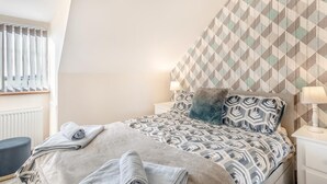Ein Schlafzimmer mit einem gemusterten Bettbezug, einem flauschigen Kissen, einer Nachttischlampe und einer Heizung.