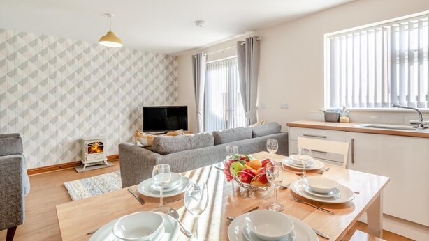 Ein modernes Wohnzimmer mit Sofa, Fernseher und Essbereich, der für eine Mahlzeit gedeckt ist.