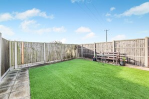 A fenced backyard with a grassy lawn, a wooden table, and a bench. - 3 Bed in Chapel St. Leonards (oc-r34145) (Chapel Saint Leonards)