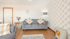 Ein Wohnzimmer mit grauem Sofa, einem kleinen Tisch mit Blumenvase, einer Lampe und einem Kamin.