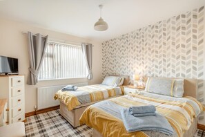 A bedroom with two beds, a TV, a radiator, and a patterned wall. - 3 Bed in Chapel St. Leonards (oc-r34145) (Chapel Saint Leonards)