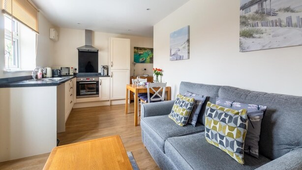 A compact living space with a kitchenette, a dining area, and a sofa with patterned cushions. - 1 Bed in Sheringham (oc-1845) (Sheringham)