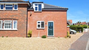 A two-story brick house with a green door, a small front garden, and a parked car. - 1 Bed in Sheringham (oc-1845) (Sheringham)