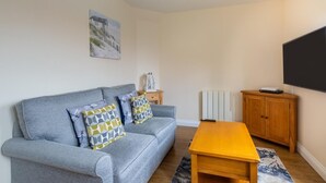 A living room with a grey sofa, wooden coffee table, and a TV on the wall. - 1 Bed in Sheringham (oc-1845) (Sheringham)