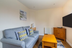 A living room with a grey sofa, wooden coffee table, and a TV on the wall. - 1 Bed in Sheringham (oc-1845) (Sheringham)