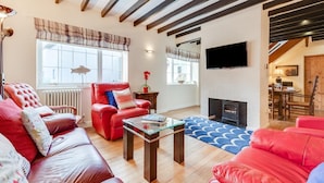 A living room with a fireplace, red leather sofas, a glass coffee table, and a TV mounted on the wall. - 3 Bed in Cromer (oc-2256) (Cromer)