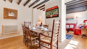 A dining area with a wooden table and chairs, a radiator, and a vintage poster on the wall. - 3 Bed in Cromer (oc-2256) (Cromer)