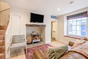 Ein gemütliches Wohnzimmer mit Kamin, Flachbildfernseher, Treppe und Fenster mit Aussicht.