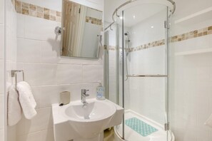 Ein Badezimmer mit Duschkabine, Waschbecken, Spiegel und Handtuchhalter.