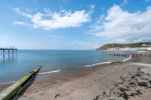 A coastal beach with a pier extending into the sea, a sandy shore, and buildings in the background. - 4 Bed in Aberystwyth (oc-bow304) (Rhos-y-garth)