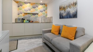 A modern kitchen with a geometric backsplash, a grey sofa with orange cushions, and a painting on the wall. - 1 Bed in Penzance (oc-u34132) (Penzance)