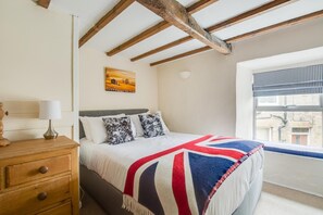 Une chambre à coucher avec un lit, une commode, un tableau et une fenêtre avec des stores.