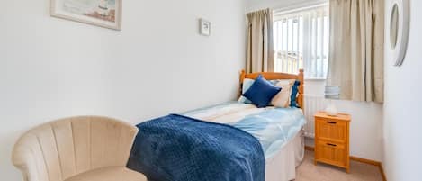 A bedroom with a bed, a chair, a bedside table, a lamp, and a window with curtains.