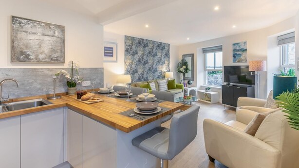 Una cocina moderna con una isla de madera, un área de comedor con sofá y un televisor en la sala.