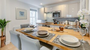 Una cocina moderna con una mesa de comedor de madera, sillas blancas y una planta en maceta.
