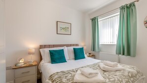 Quarto com uma cama, duas mesas de cabeceira, um criado-mudo, uma janela com cortinas e um quadro na parede.