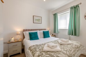 Ein Schlafzimmer mit einem Bett, zwei Nachttischen, einem Fenster mit Vorhängen und einem Wandbild.