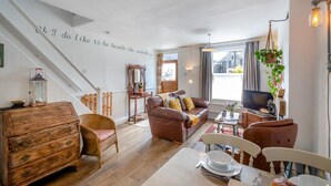 Een gezellige woonkamer met een trap, een bruine leren bank, een houten dressoir en een eettafel gedekt voor twee personen.
