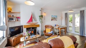 Een gezellige woonkamer met een open haard, een televisie, een eethoek met een tafel en stoelen, en een groot raam met gordijnen.