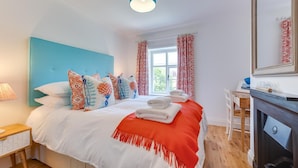 A modern bedroom with a blue headboard, patterned pillows, a red throw blanket, and a bedside table with a lamp. - 4 Bed in Northrepps (oc-2332) (Northrepps)