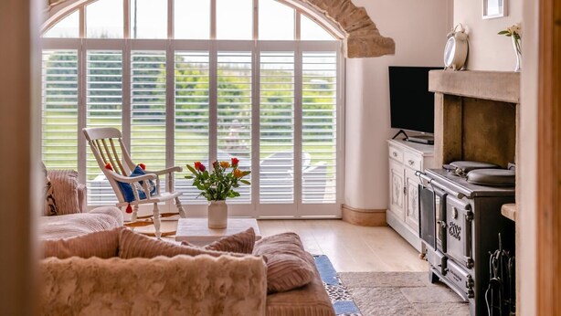 Ein Wohnzimmer mit einer Couch, einem Sessel, einem Fernseher, einem Kamin und einem großen Fenster mit Jalousien.