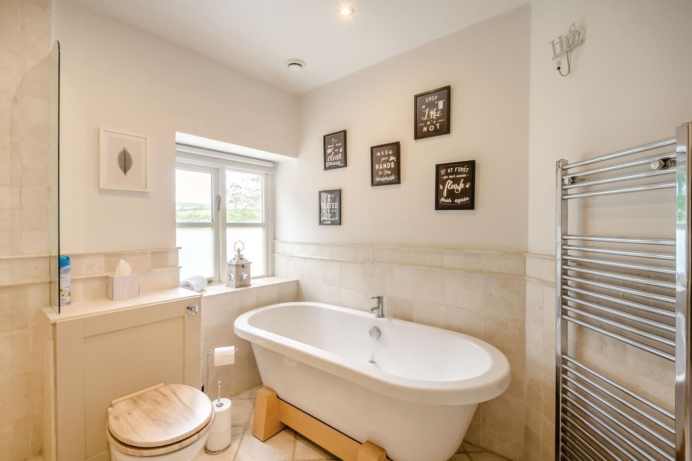 A modern bathroom with a freestanding bathtub, a toilet, a vanity with a mirror, and a window providing natural light.